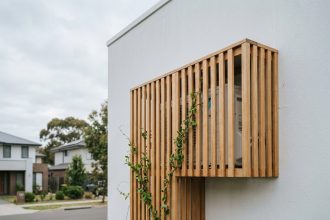 Climatisation murale dissimulée derrière un panneau en bois à lamelles sur façade blanche d'une maison moderne